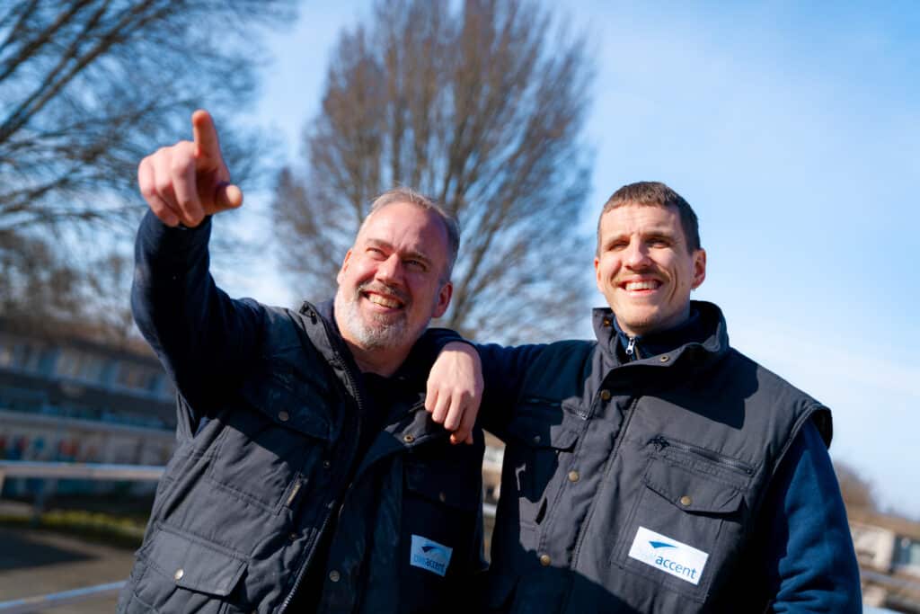 Glimlachende dakdekkers van DAKaccent werken samen met uitrusting op een zonnige dag