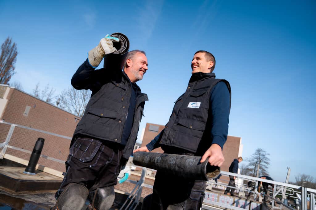 Twee vrolijke DAKaccent dakdekkers werken samen aan dakbedekking"